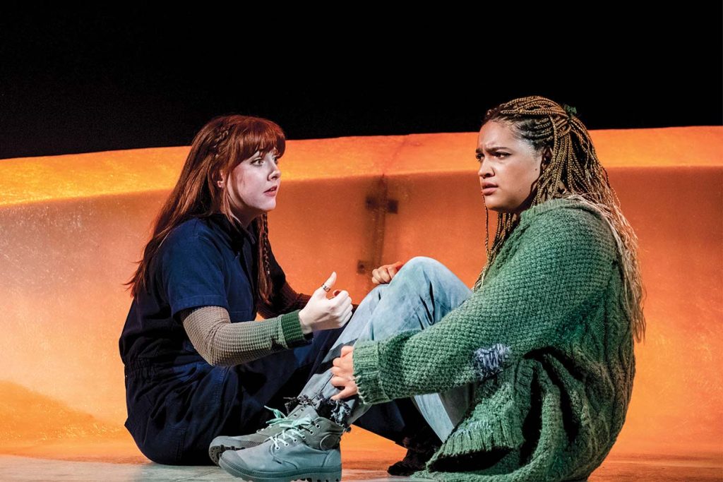 Two actors seated on the floor in tense discussion