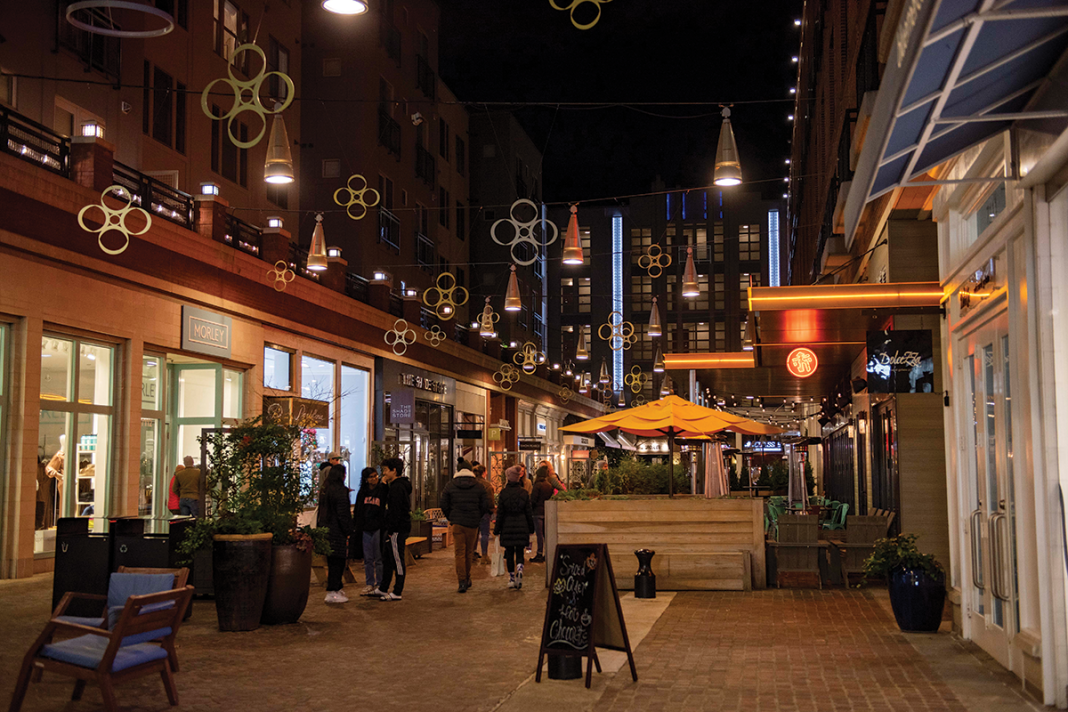 Shops along Bethesda Lane with people walking and shopping at night.