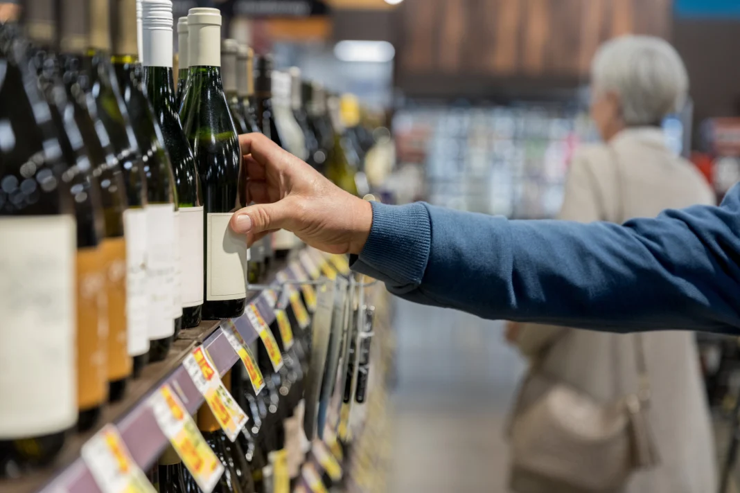Photo of man's hand reaching for wine bottle in supermarket